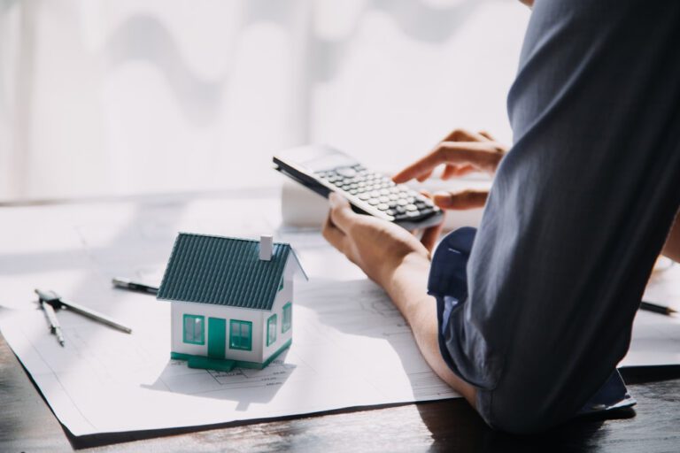 Homem realizando cálculos de imóvel em uma calculadora com um modelo de casa ao seu lado.