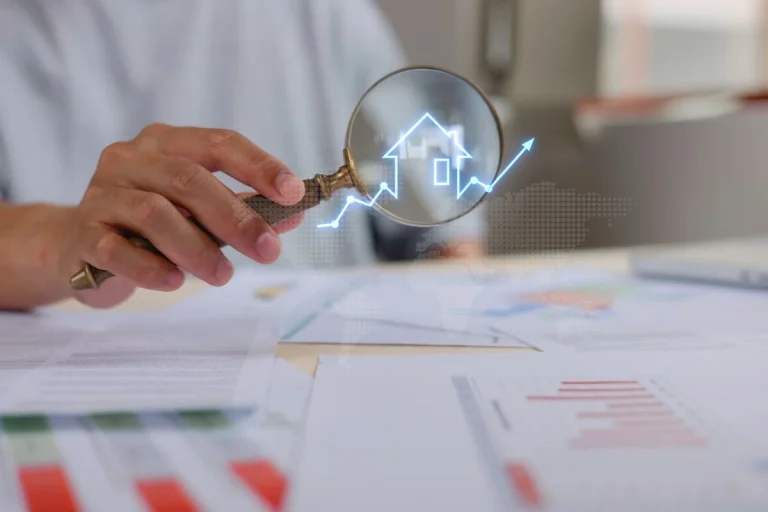 Profissional analisando documentos do mercado imobiliário com uma lupa sobre uma representação de uma casa e gráfico de crescimento, ilustrando o acompanhamento de métricas de vendas e a valorização de imóveis.